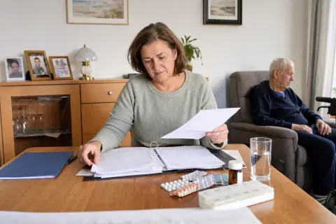 Arztbrief und Medikamentenplan – Antrag „Arztbrief und Medikamentenplan – Antrag“: Eine Angehörige und eine pflegebedürftige Person ordnen gemeinsam medizinische Unterlagen und Hilfsmittel.