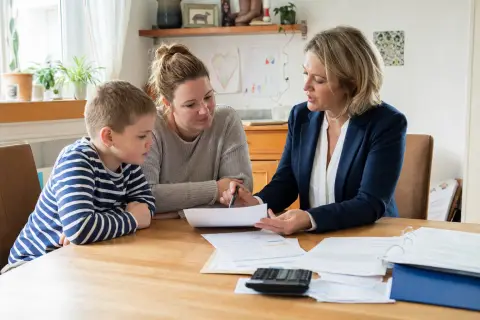Pflegegrad für ein Kind – Kosten „Pflegegrad für ein Kind – Kosten“: Eltern und eine Fachberaterin besprechen zu Hause die Unterstützung eines pflegebedürftigen Kindes.