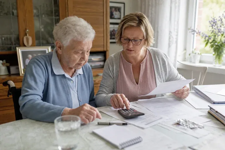 „Pflegetagebuch für die Begutachtung – Kosten“: Eine Angehörige und eine pflegebedürftige Person prüfen gemeinsam Pflegeunterlagen an einem Tisch.