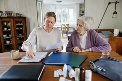 Pflegeunterstützungsgeld – Unterlagen „Pflegeunterstützungsgeld – Unterlagen“: Eine pflegende Angehörige prüft Unterlagen zur Vereinbarkeit von Beruf, Absicherung und Pflege.